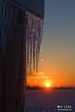 Close-up vertical of icicles on a road sign with the setting sun after an ice storm