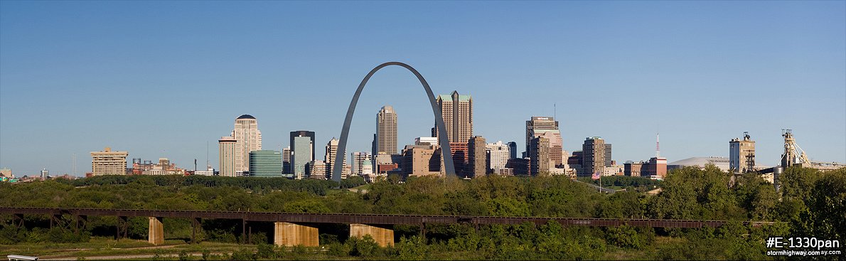 Panorama of the St. Louis skyline and Gateway Arch with green trees and blue sky